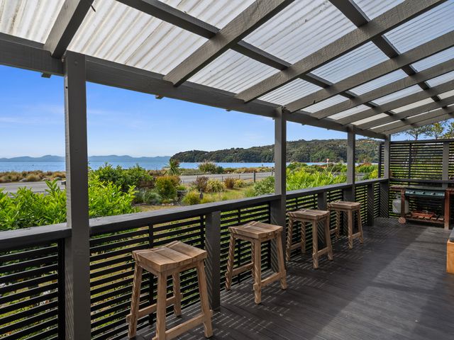 An outdoor terrace with stools and a view of the water at Raisin Town - Marahau Bach in Marahau