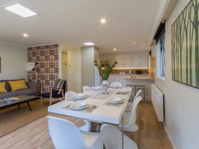 A dining table set with white plates and glasses next to a kitchen and living area at Alchemy Cottage - Arrowtown Holiday Home in Arrowtown