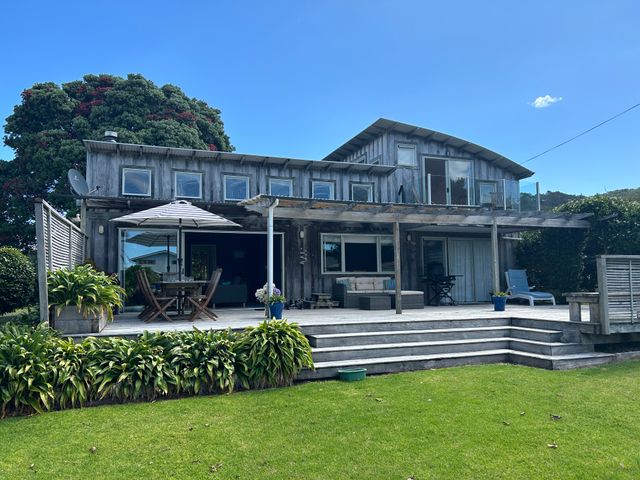 A wooden two-story house with a large deck and outdoor seating on a grassy lawn at Coro Beach Haven - Hahei Holiday Home