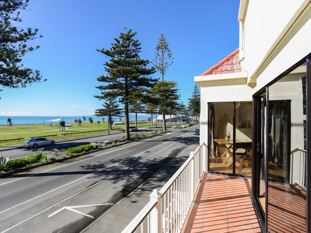 A balcony overlooking a road with trees and a grassy area by the sea at Marine Parade Magic - Napier Holiday Home in Marewa