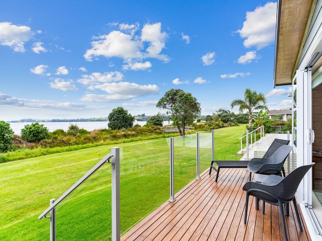 An outdoor area with a deck and chairs overlooking a grassy area and water at Beachfront Escape - Snells Beach Holiday Home in Matakana