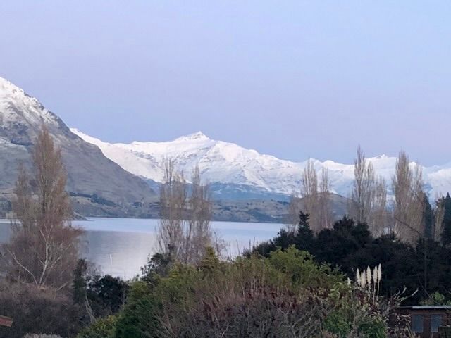 A view of mountains and a lake with trees in the foreground at Lakeside Escape - Wanaka Holiday Bach Wanaka
