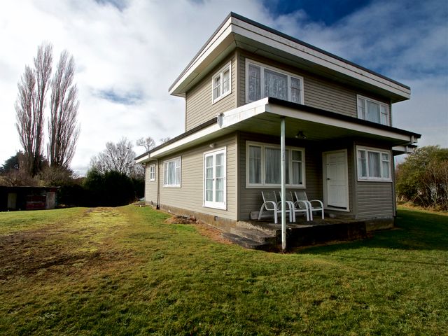 A two-story house with a porch and two chairs on grass at Raetihi Cottage- Raetihi Holiday Home in Raetihi