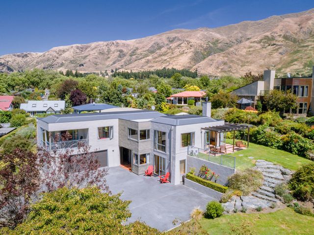 A modern two-story house with a driveway and garden surrounded by trees and mountains at Sargood Splendour - Wanaka Holiday Home Wanaka