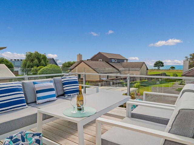 An outdoor seating area with a table glasses and a bottle overlooking houses and the sea at Coastal Pearl Matarangi Holiday Home in Matarangi