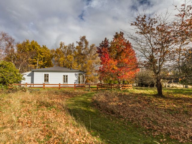 A white house with a brown fence surrounded by trees with autumn leaves at Kaha Cottage - Rangataua Holiday Home in Ohakune