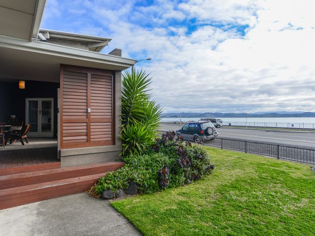 A house porch with a wooden door next to a garden and street with cars near water at Breakwater Cottage - Napier Holiday Home in Bluff Hill