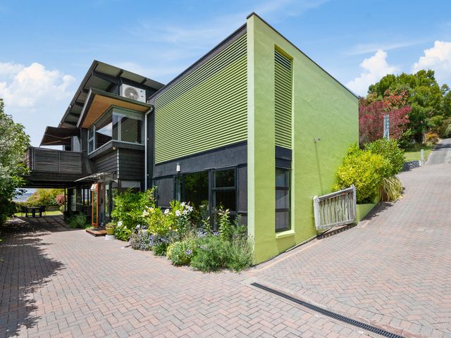 A modern house with green and black exterior walls a paved driveway and garden beds at Acacia Bay Retreat - Acacia Bay Holiday Home in Acacia Bay