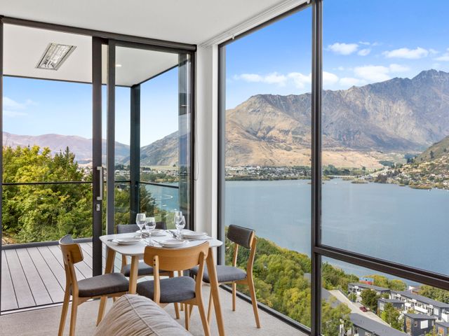 A dining area with a white table and four chairs next to large windows overlooking a lake and mountains at Sierra Views - Queenstown Holiday Home in Queenstown