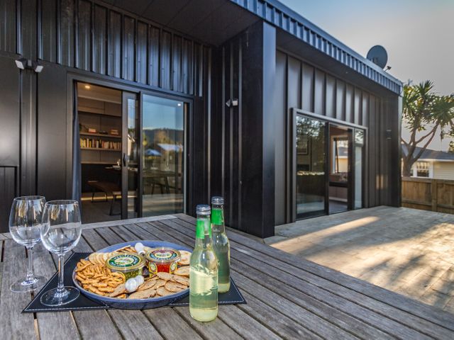 An outdoor wooden table set with a platter of crackers and two bottles with two wine glasses in front of a modern building with large windows at Ohakune Snowhaus Ohakune