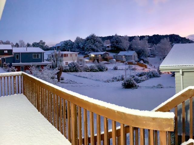 A snowy residential neighborhood with houses trees and a wooden deck covered in snow at Turoa Lookout - Ohakune Holiday Home in Ohakune