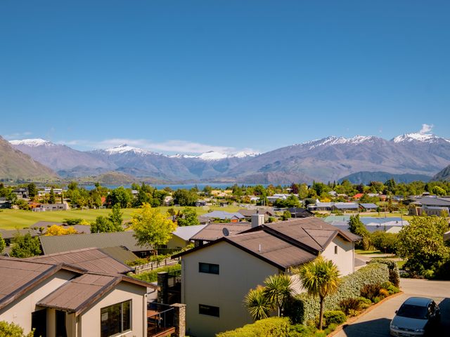 A residential area with houses and trees with snow-capped mountains and a lake in the background at Kings View - Wanaka Holiday Home in Wanaka