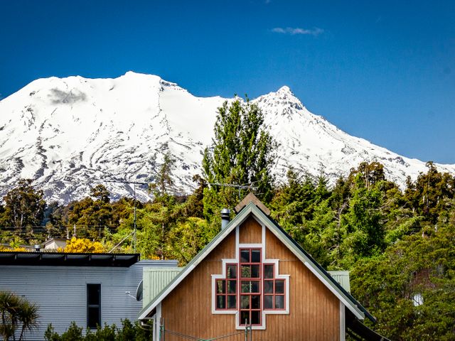 A wooden house with decorative windows in front of snow-covered mountains and trees at The Gingerbread House - Ohakune
