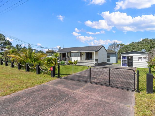 A fenced driveway leading to a single-story house with a porch and a separate small building in the yard at Bream Bay Sands - Ruakaka Holiday Home Ruakaka