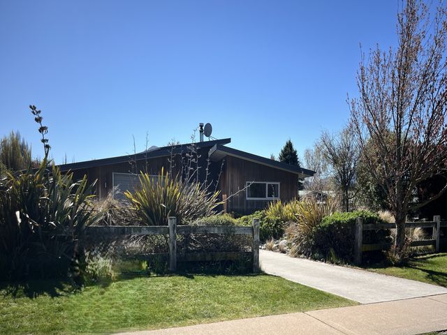 A house with wooden exterior surrounded by bushes and a wooden fence with a concrete driveway at Hikuwai Family Retreat - Albert Town Holiday Home in Wanaka