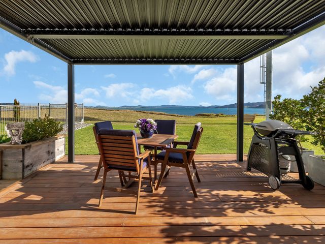 An outdoor patio with wooden table and chairs a barbecue grill and ocean view at The Leading Light - One Tree Point Holiday Home in One Tree Point