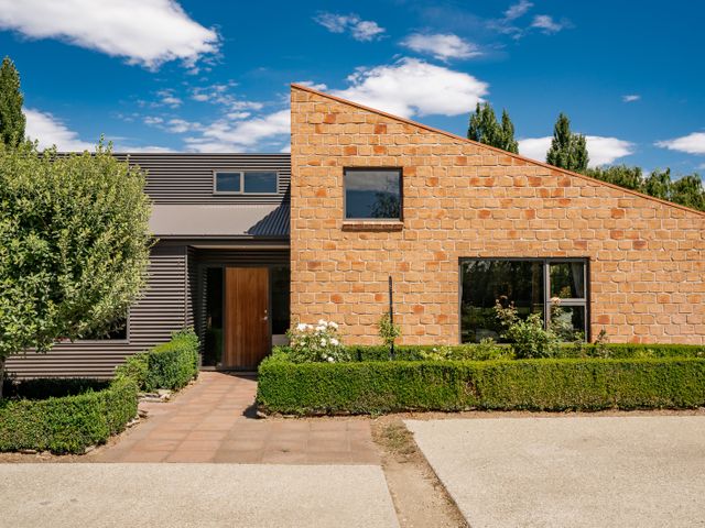A house with a stone and metal exterior with hedges and a tiled walkway at Edgewater Escape - Cromwell Holiday Home in Cromwell