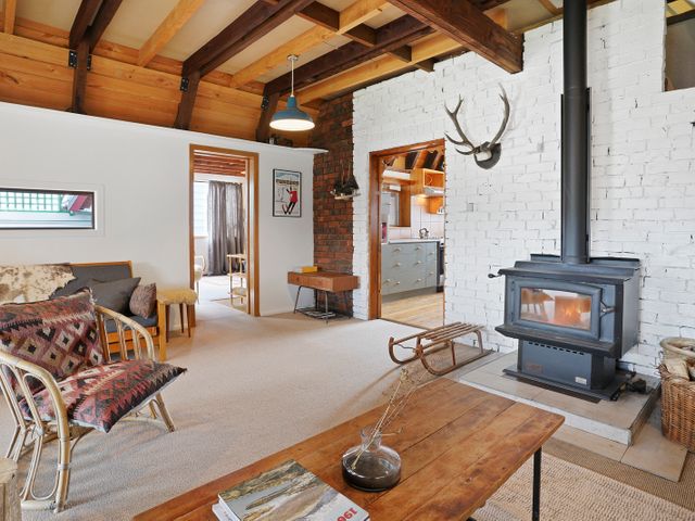 A living room with a wood stove and antlers mounted on a white brick wall at Snow Chalet in Fairlie