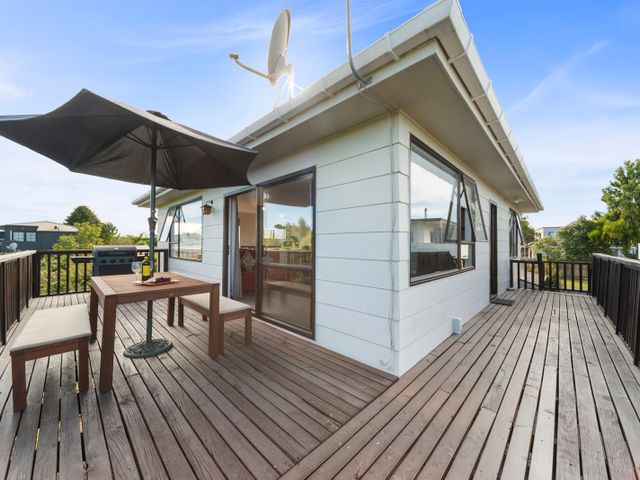 A wooden deck with a table, benches, umbrella, and barbecue grill at Rainbow Lake House - Lake Taupo Holiday Home in Rainbow Point