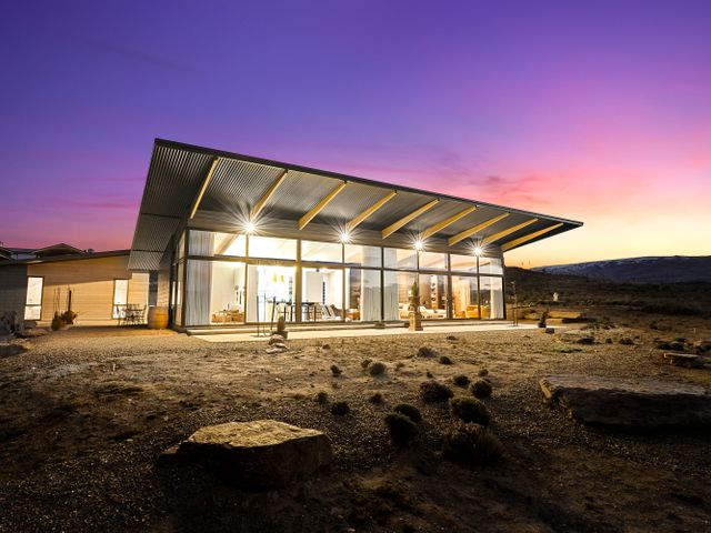 A modern house with large glass windows and a slanted roof at sunset at Bridge Hill Beauty Alexandra Holiday Home in Alexandra
