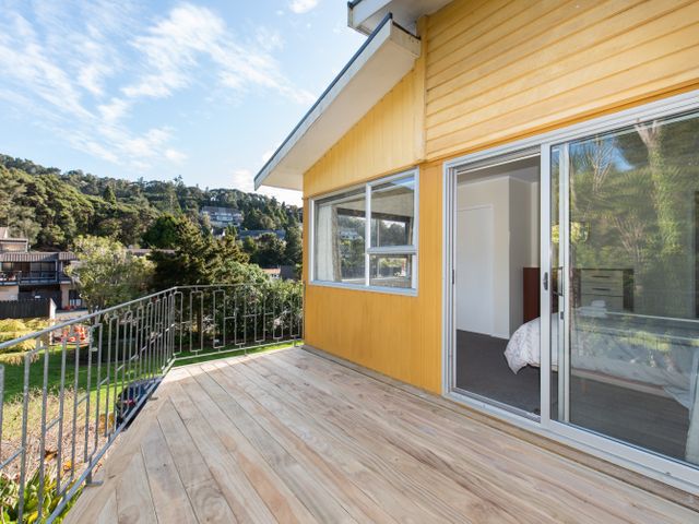 A wooden deck balcony with metal railing outside a yellow house in a residential area at Knight's Retreat - Paihia Holiday Home Paihia