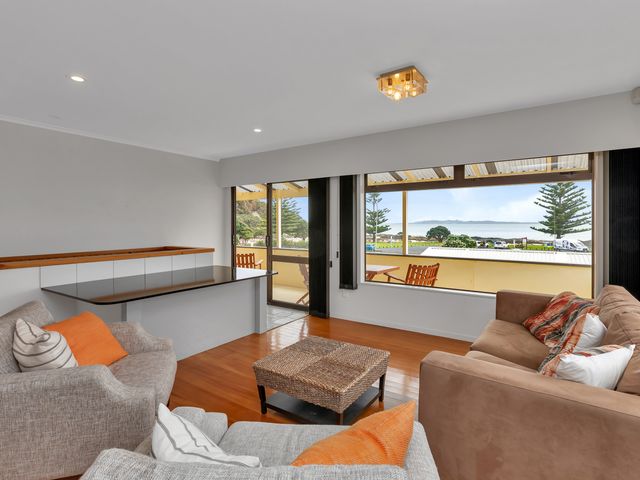 A living room with sofas a wicker coffee table and a large window overlooking a balcony and the sea at Seaside on Stratford - Cable Bay Holiday Home