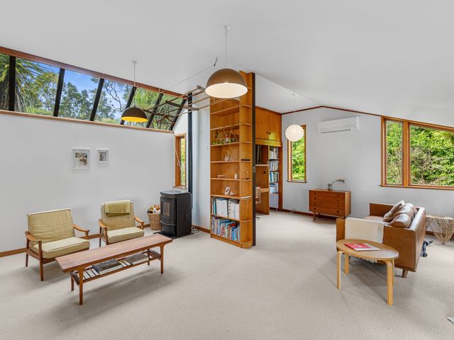 A living room with chairs a coffee table a bookshelf and a sofa at Treetop Sanctuary - Titirangi Holiday Home Titirangi