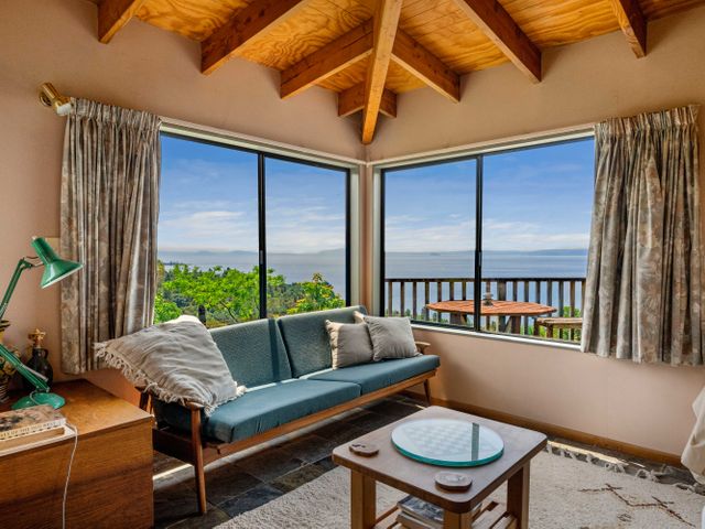 A living room with a blue sofa pillows a small wooden table with a chess board and large windows showing a water view at Pukawa Paradise - Pukawa Holiday Home in Pukawa Bay