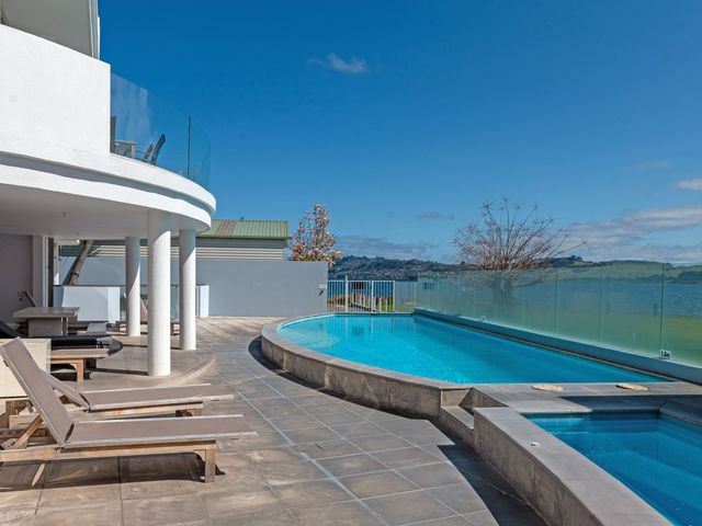 An outdoor pool area with lounge chairs and a glass fence overlooking a body of water at Waimahana 5 - Taupo Holiday Apartment in Waipahihi