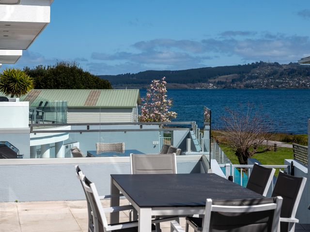 An outdoor dining table with chairs on a balcony overlooking a body of water with trees and hills in the background at Waimahana 5 - Taupo Holiday Apartment in Waipahihi