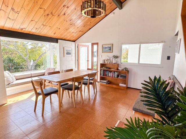A dining room with a wooden table and six chairs a built in bench under a window and a bookshelf at Sunset Sanctuary - Havelock North Holiday Home in Havelock North