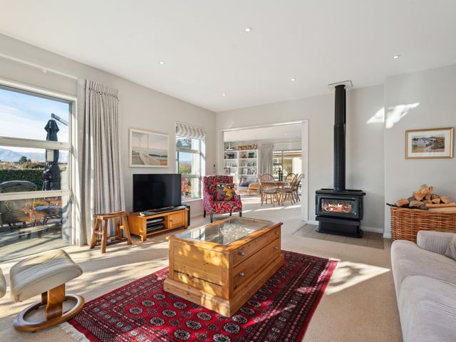 A living room with a fireplace television wooden table red rug and armchairs at Tranquil on Ribbonwood - Wanaka Holiday Home in Wanaka