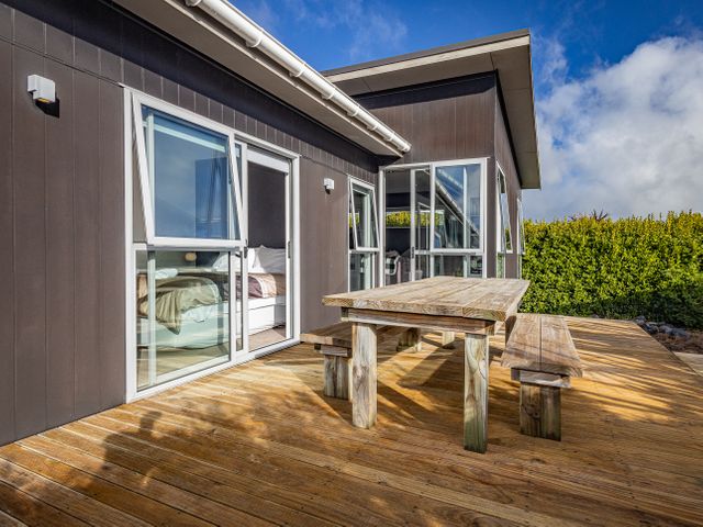 An outdoor wooden deck with a wooden table and benches beside a modern house with large windows at Snow-Vannah Ohakune Holiday Home