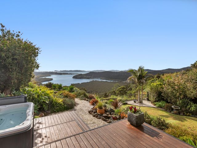 A backyard with a hot tub a wooden deck and plants overlooking a body of water and hills at Sunrise Lookout - Paihia Holiday Home in Haruru 3km from Paihia