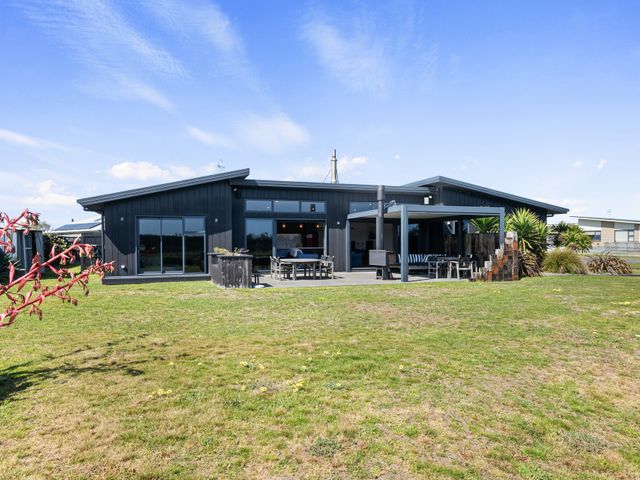 A single-story house with a black exterior wall a patio area with outdoor furniture and a lawn in front at Surfing Fox - Foxton Beach Holiday Home in Foxton