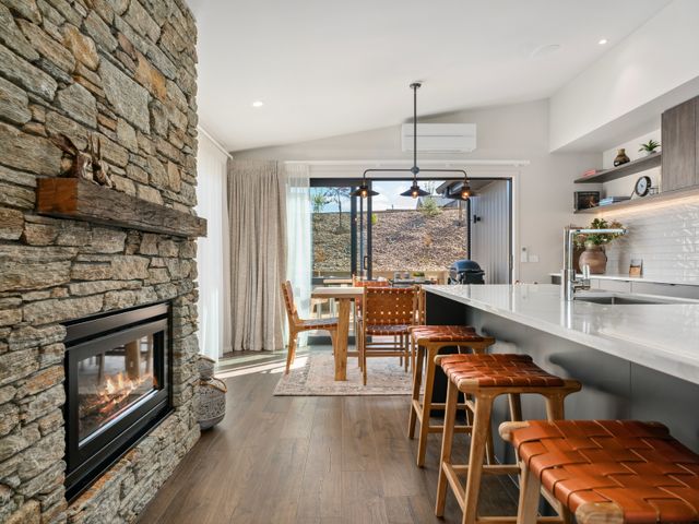 A kitchen and dining area with stone fireplace wooden stools and sliding glass doors at 86 on Kirimoko - Wanaka Holiday Home in Wanaka