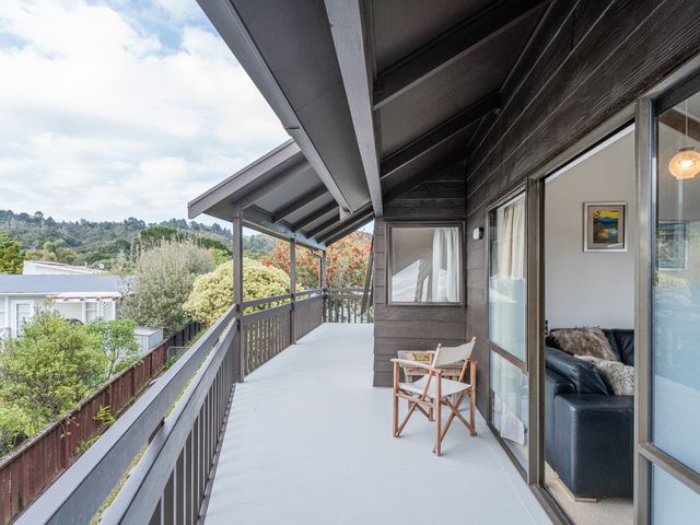 A covered balcony with a wooden chair overlooking trees and neighboring houses at Whanga Bach - Whangamata Holiday Home in Whangamata