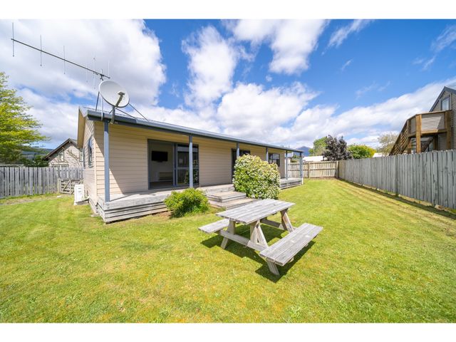 A backyard with a wooden picnic table and a beige house with a porch and satellite antenna Cosy Lakeside - Manapouri Holiday Home in Manapouri