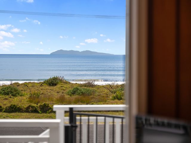 A view of the ocean with an island in the distance and grassy dunes in front seen through a balcony railing at Kiwi Beach Bach Waihi Beach