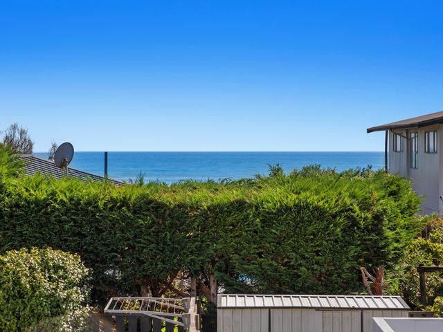 A backyard with green bushes a shed and houses with an ocean view at Sunny Daze - Ohope Beach Holiday Home in Ohope Beach