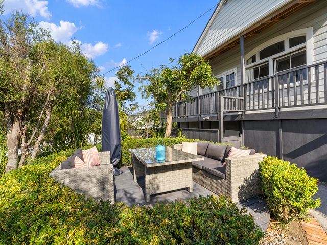 An outdoor patio with wicker sofas and a glass-top table surrounded by bushes at Heritage Charm - New Plymouth Holiday Home in Moturoa