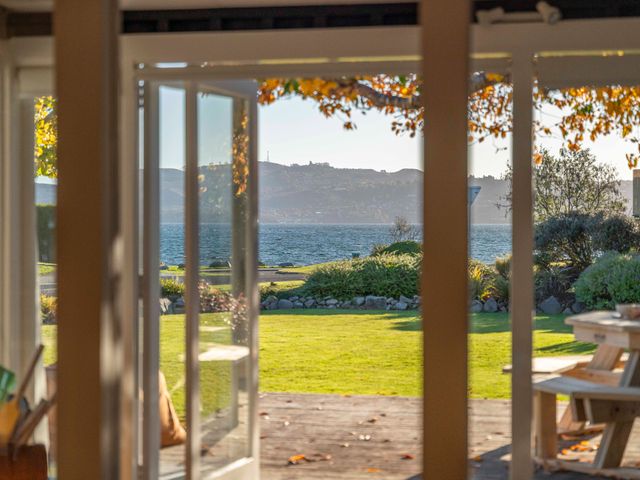 A view through open doors onto a lawn and lake with hills in the background at Waterside Bliss Taupo Central