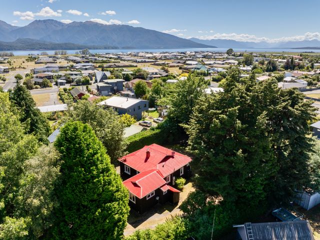 A house with a red roof surrounded by trees near a lake at Fiordland Hideaway - Te Anau Holiday Home