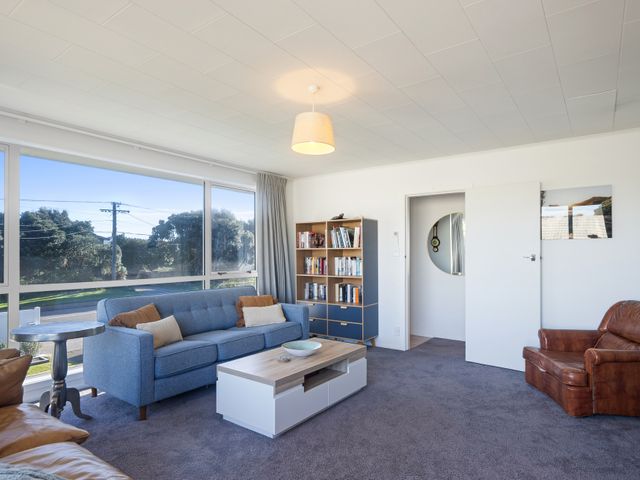 A living room with a sofa and bookshelf at The Beach Base - Paraparaumu Holiday home Paraparaumu