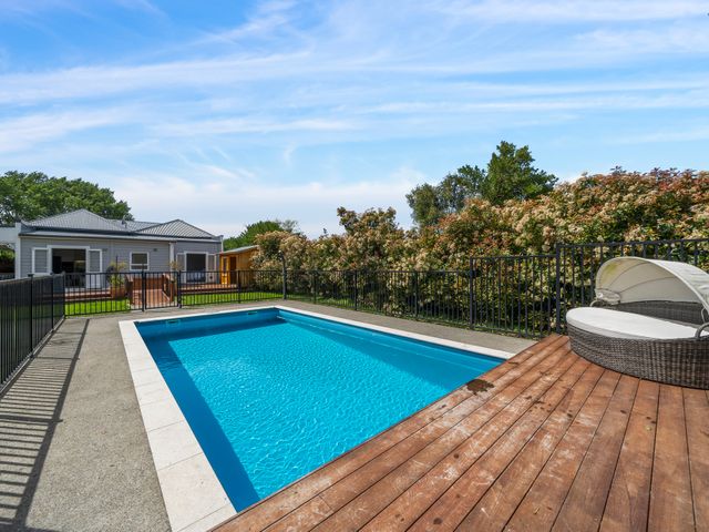 A swimming pool with a wooden deck and a house in the background at the property