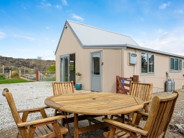 An outdoor seating area with a wooden table and chairs near a house in a rural setting
