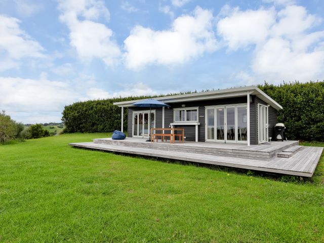 A cabin with a deck and outdoor furniture at Mangawhai Holiday Unit in Kaiwaka