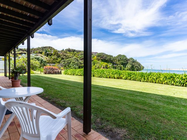 A table and chair on a veranda overlooking grass and the sea at Mangawhai Marvel - Mangawhai Heads