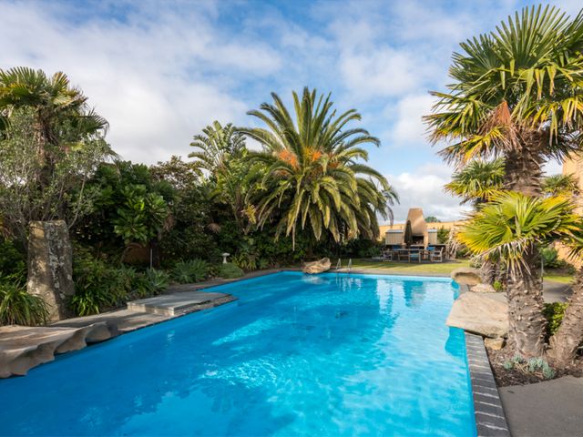 An outdoor area with a swimming pool and palm trees at La Belle Retreat - Ruakaka Holiday Apartment, Ruakaka