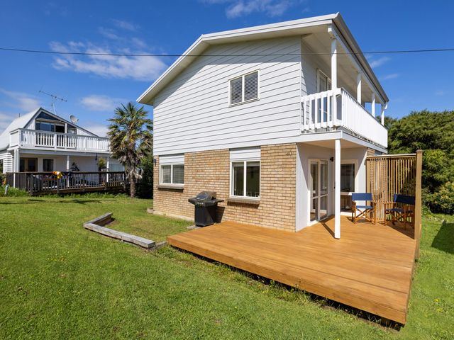 A two-story house with a wooden deck and grill at Raglan Holiday Home in Raglan